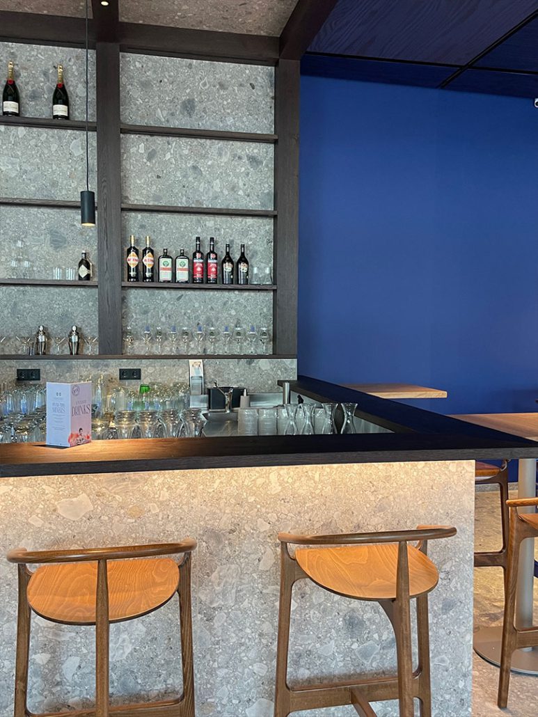 eli-schwabing_h05 Barbereich im Restaurant ELI Schwabing mit Barhockern und Flaschenregal.