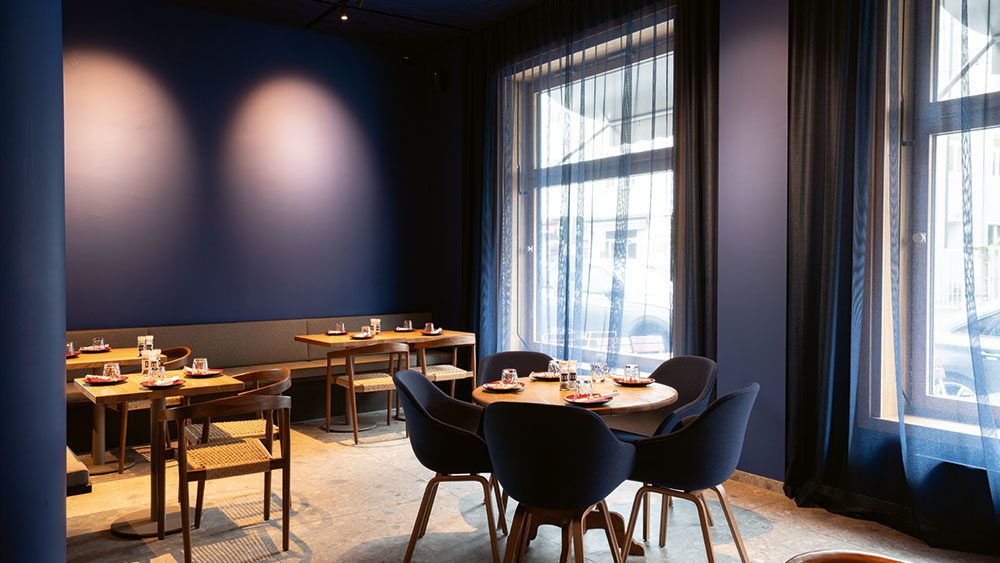 eli-schwabing_q4 Gastraum im Restaurant ELI Schwabing mit eingedeckten Tischen am Fenster und Tageslicht.