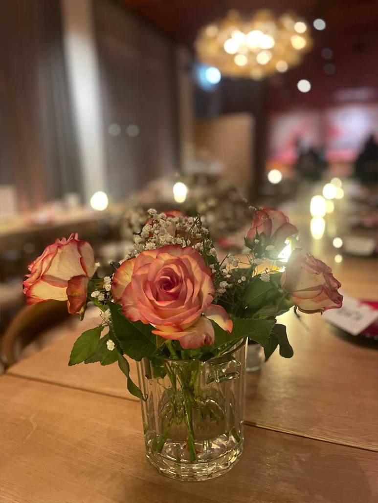 Blumendekoration auf einer langen Veranstaltungstafel im Restaurant ELI Schwabing mit stimmungsvoller Beleuchtung.