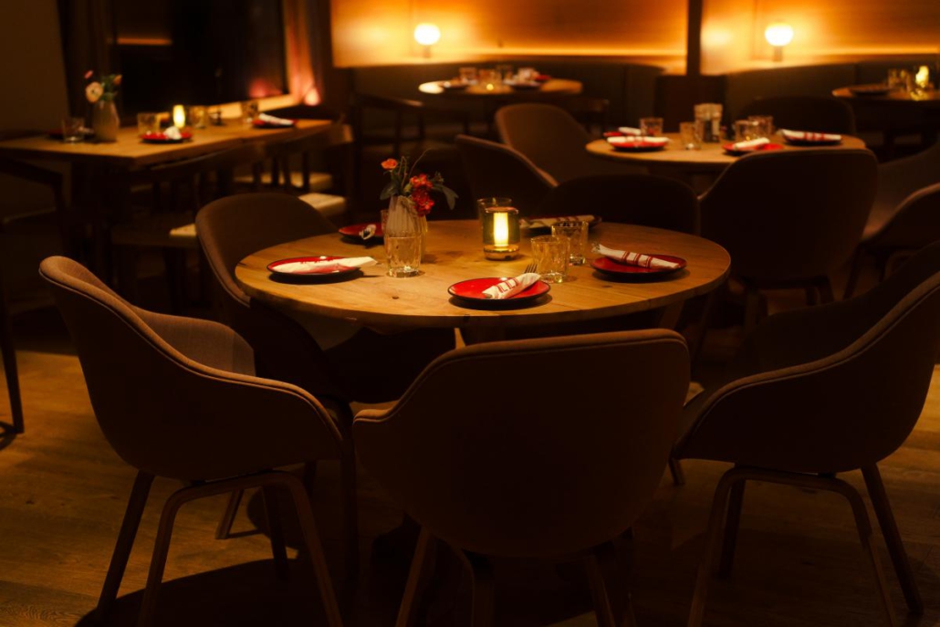 Gemütlich gedeckter Restaurantbereich mit runden Tischen und stimmungsvoller Beleuchtung im ELI Schwabing.